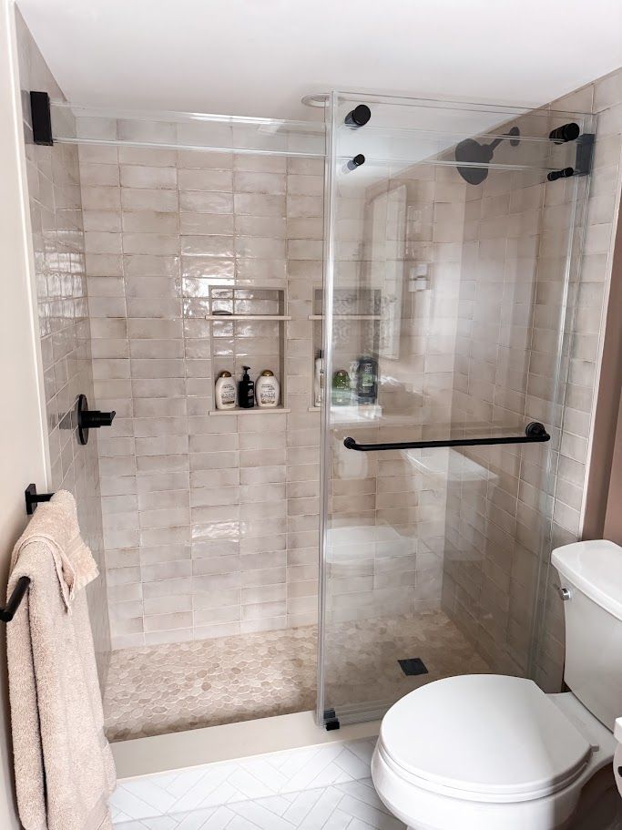 Modern beige tiled bathroom with glass shower, built-in shelves, towel, and toilet