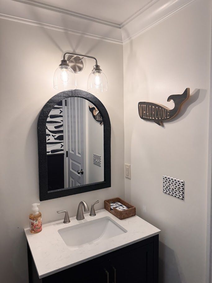 Small bathroom vanity with arched mirror, wall sconce, white sink, and decorative fish wall art.