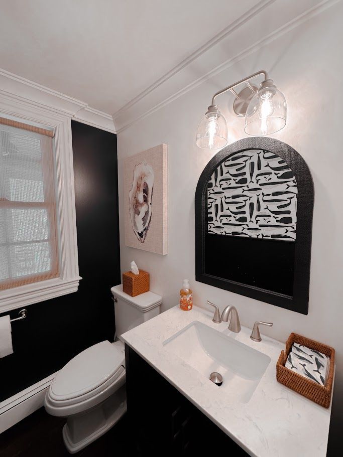 Small modern bathroom with black-and-white walls, sink, toilet, window, and wall art.