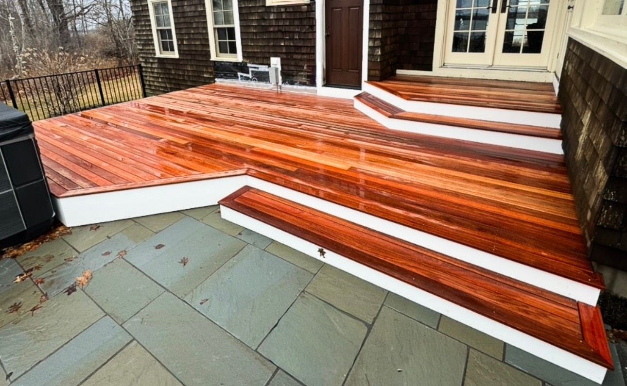 Wooden deck and steps with white snow-like edging beside a house, viewed from a patio.