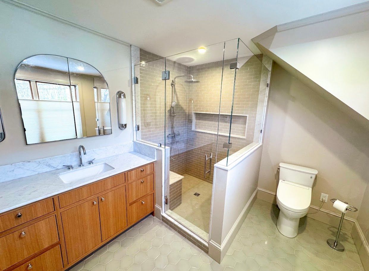 Modern bathroom with double sink, glass shower, and toilet under a slanted ceiling
