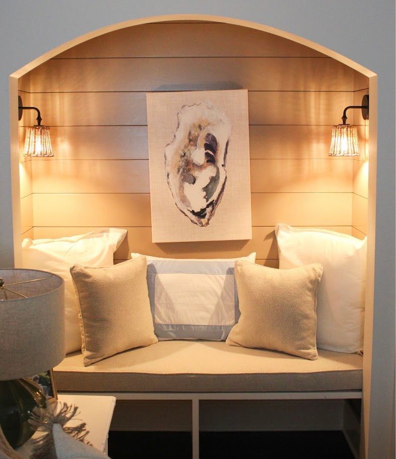 Cozy alcove daybed with pillows, warm sconces, and abstract wall art in a soft neutral room