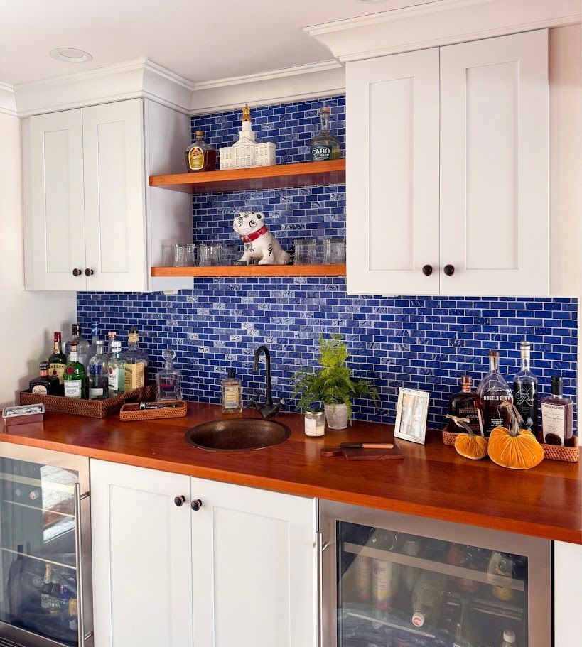 White kitchen with blue tile backsplash, wooden countertops, open shelves, and potted plants
