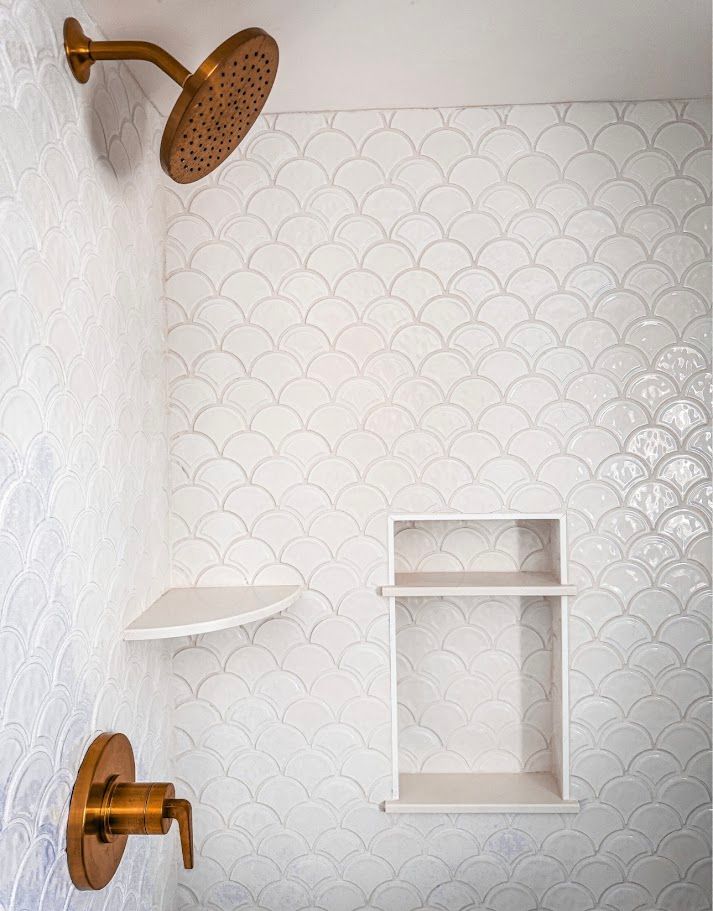 White tiled shower with brass showerhead and fixture, small shelf, and recessed niche.
