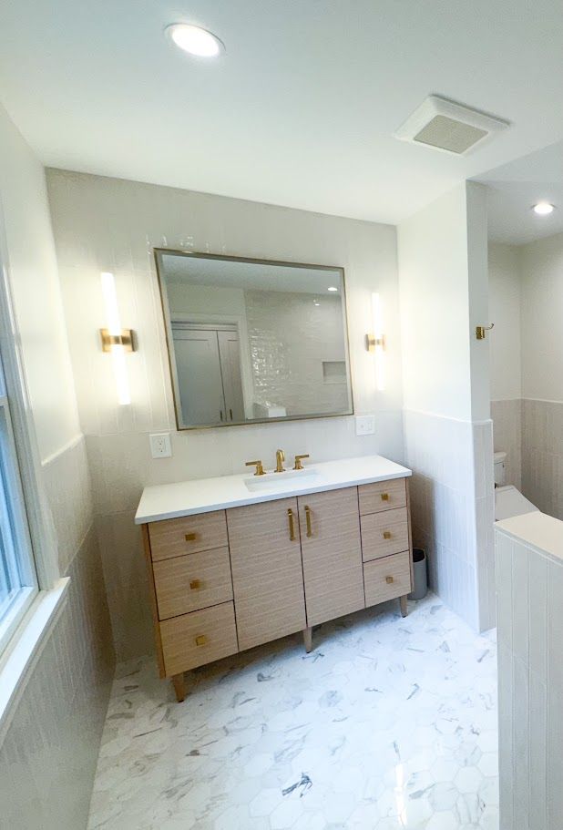 Bright bathroom with vanity, mirror, and toilet, featuring white tile and light wood cabinets