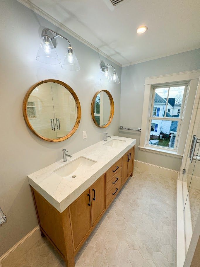 Bright bathroom vanity with wood cabinets, large mirror, white walls, and marble-look floor.