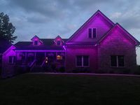 Stone house lit with purple lights at dusk, with glowing roofline and dormer windows.