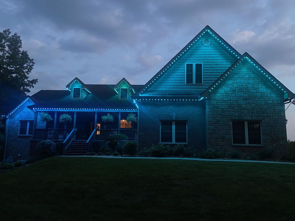 House at dusk with blue accent lights and a lit front porch under a cloudy sky
