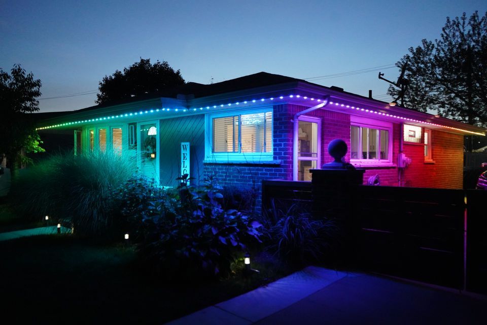 House at night lit with colorful blue, green, and pink LED lights along the roofline.
