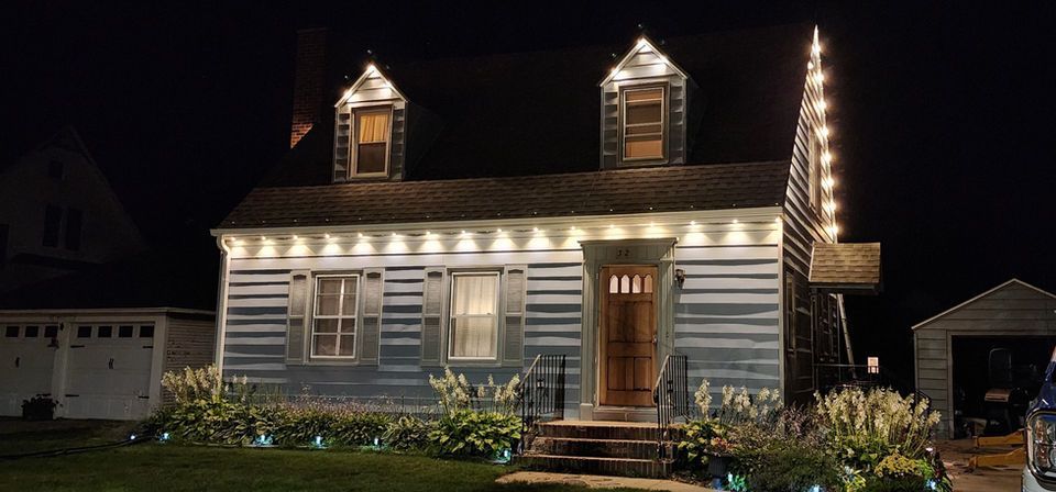 House at night decorated with warm white Christmas lights and lit dormer windows