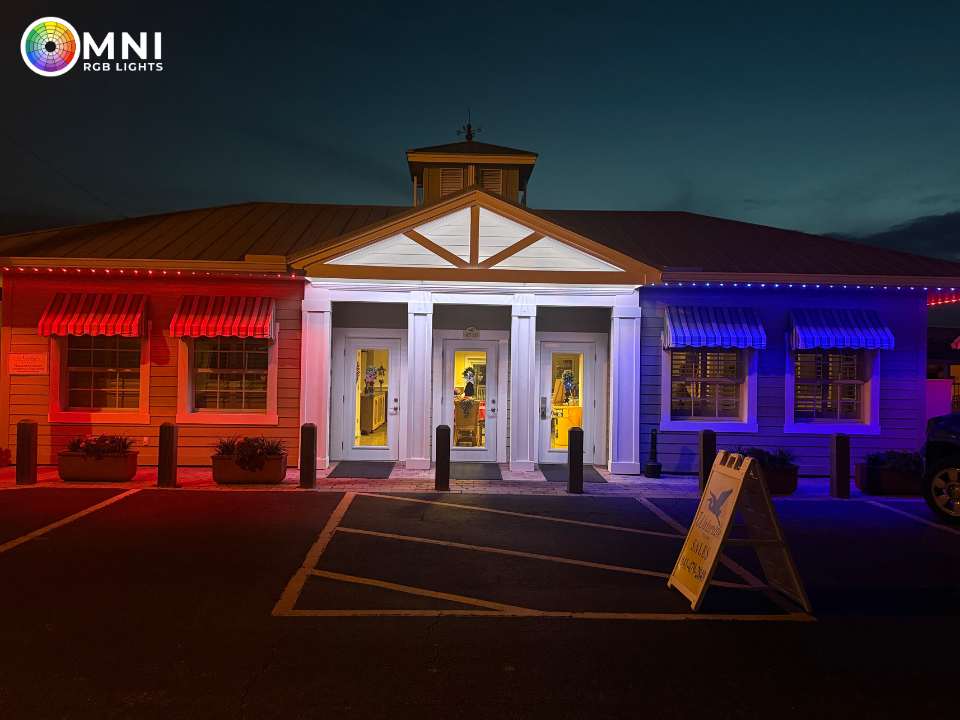 Building lit red and blue at night, with a white central entrance and parking lot in front