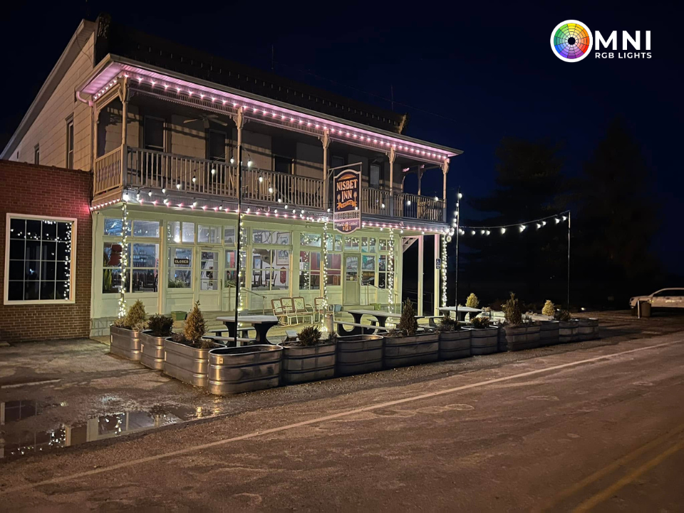 Nighttime view of a lit two-story restaurant with outdoor seating and string lights along a wet street