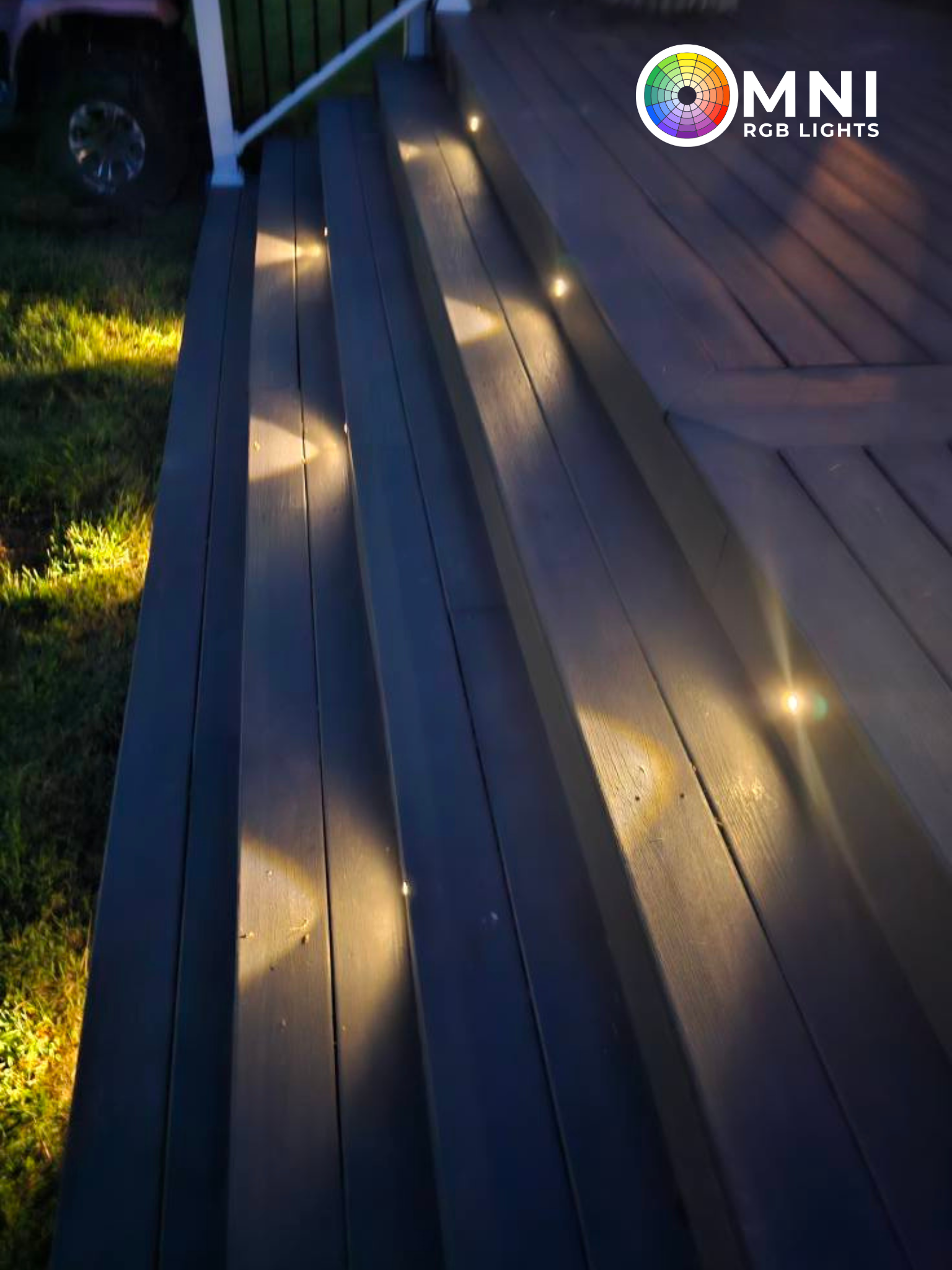 Wooden deck steps lit by small warm lights at dusk, with grass beside them