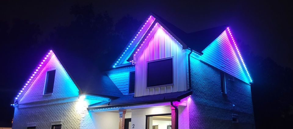 House with colorful purple and blue holiday lights on the roof at night