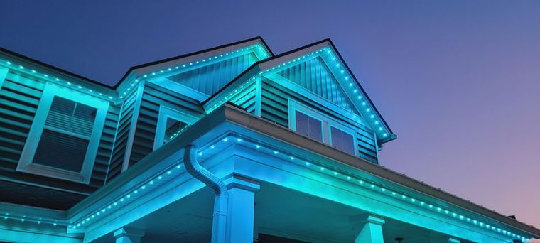 Blue-lit house exterior at dusk with illuminated roof and windows