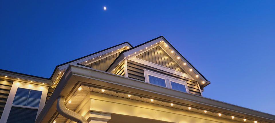 Lit-up house roof at dusk under a deep blue sky with a bright moon.