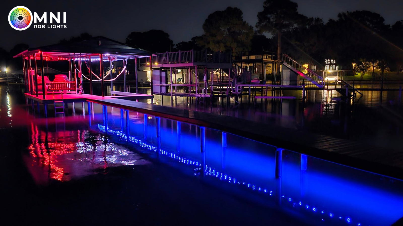 Nighttime waterfront pavilion with pink and blue lights reflecting on the water