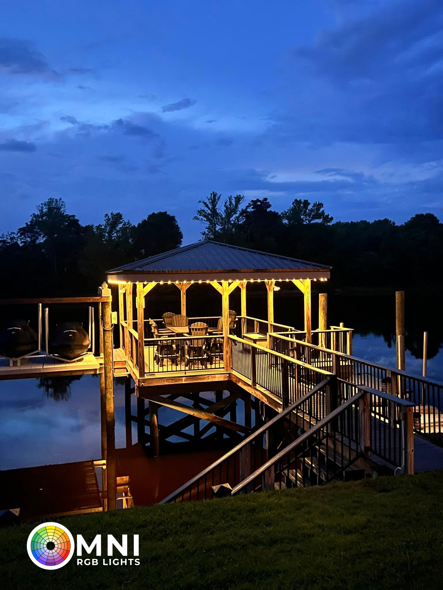 Lit gazebo over a dock at dusk, glowing warmly beside a calm lake and trees