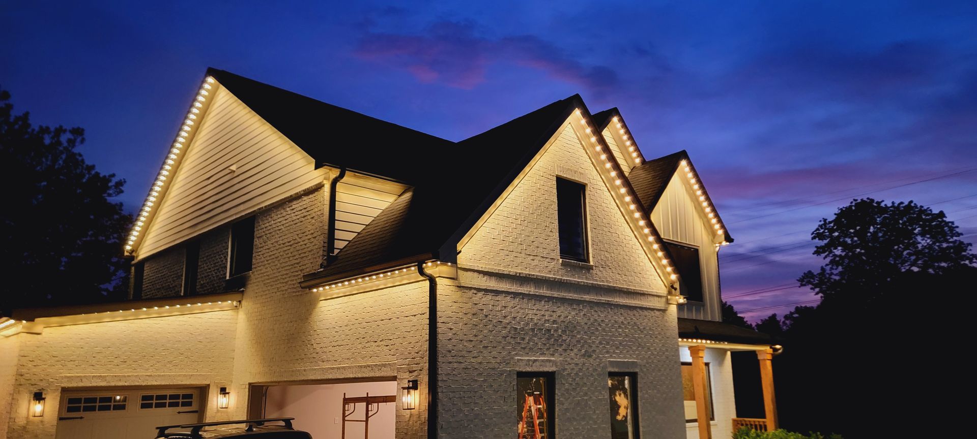 Well-lit stone house at dusk with peaked roofs and warm exterior lights