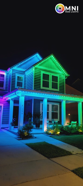 Neon-lit suburban house at night glowing blue, green, and purple with a lit porch and driveway