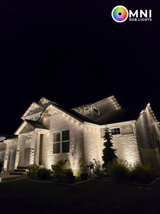 Well-lit white house at night with warm holiday lights outlining the roof and facade.