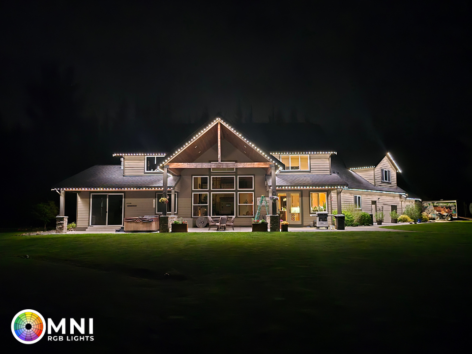 Well-lit modern house at night with stone and wood exterior, glowing windows, and a dark lawn