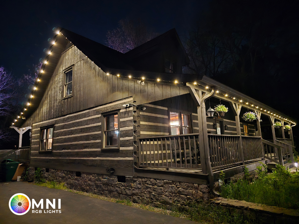 Rustic log cabin at night with warm string lights and a covered porch in a wooded setting
