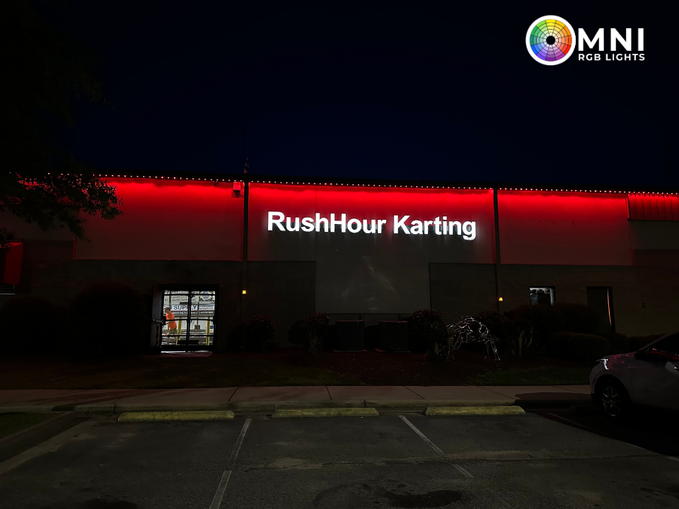 Nighttime exterior of RushHour Karting with red-lit signage and a parking lot in front