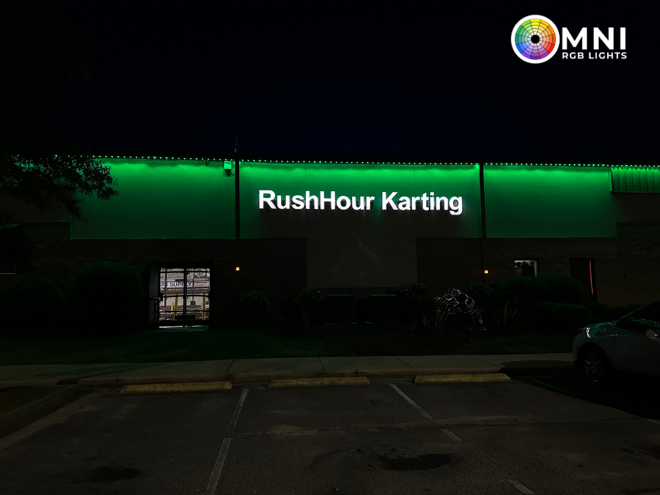 RushHour Karting storefront at night, lit with green neon signage and dark parking lot in front