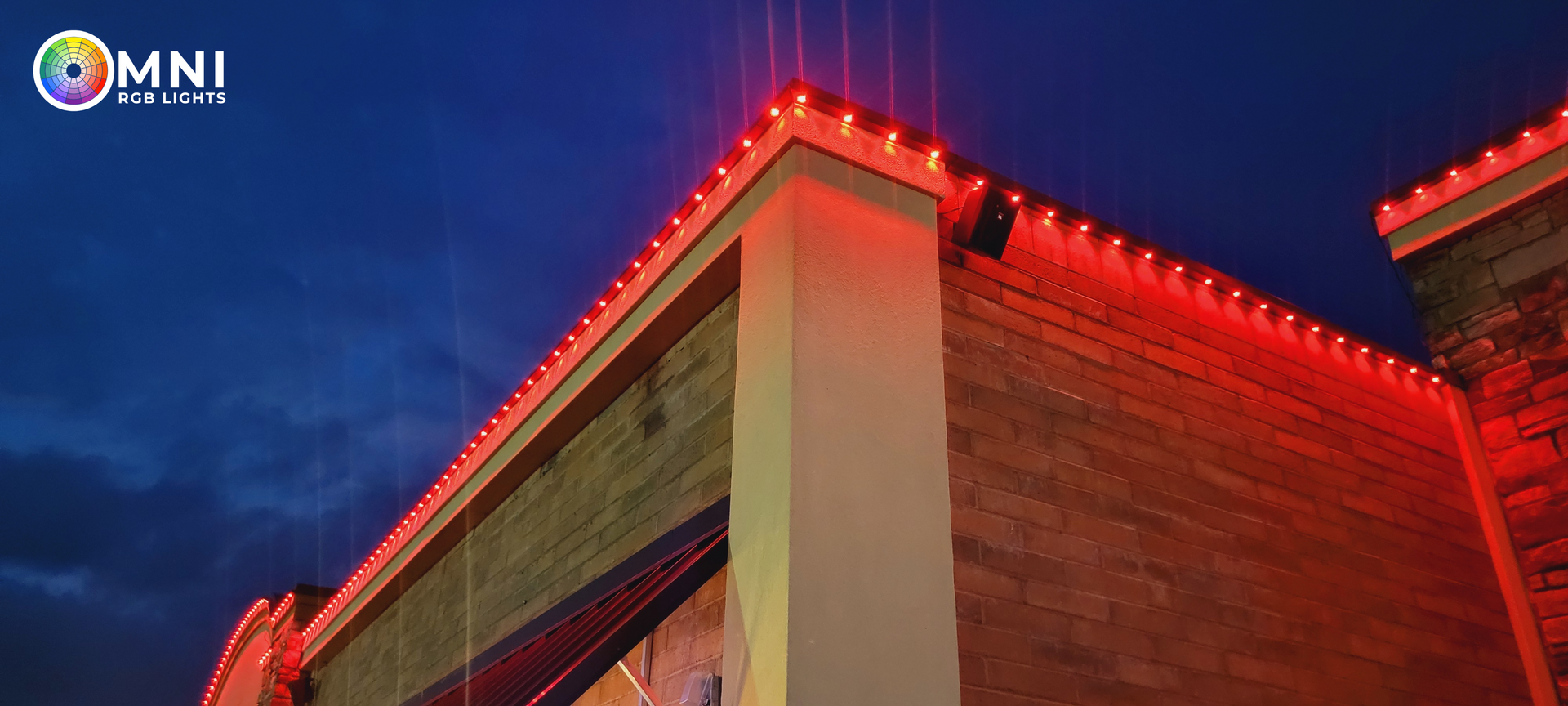 Illuminated building corner with red rooftop lights against a deep blue sky