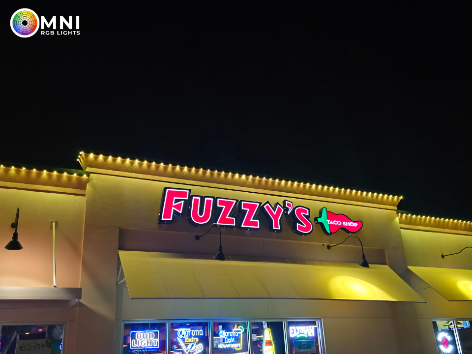 Night view of Fuzzy’s restaurant sign glowing pink and green above a lit storefront
