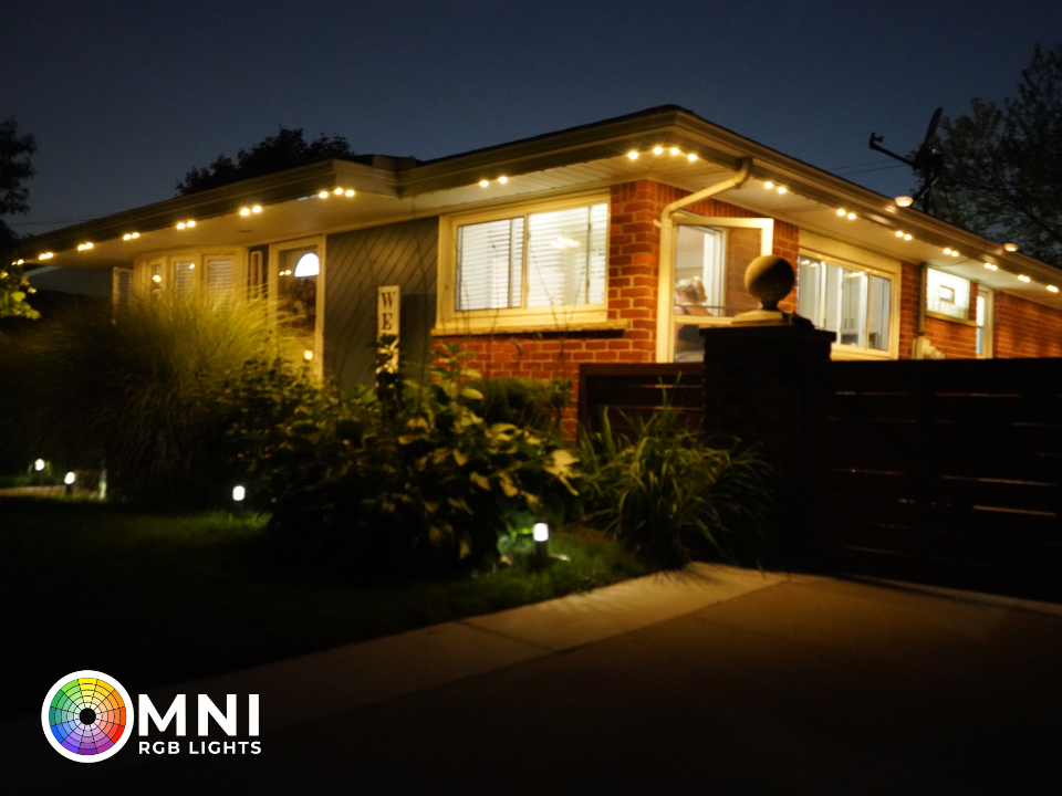Well-lit modern house at night with warm porch lights and a landscaped front yard