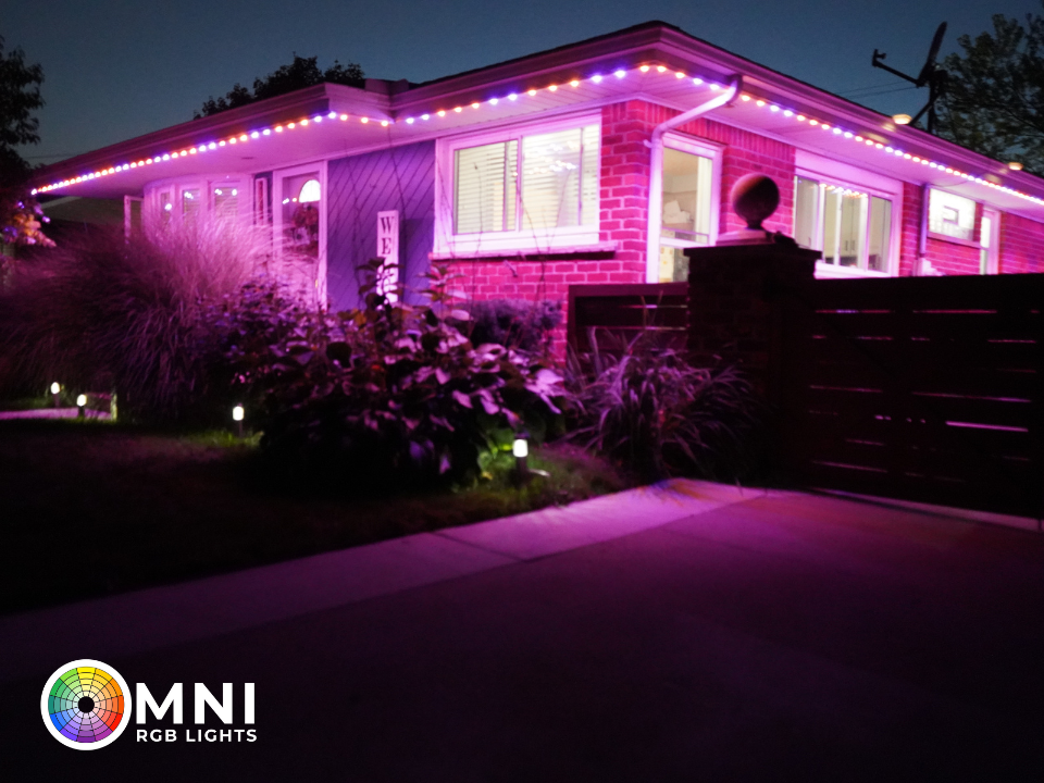 House exterior lit with pink-purple LED lights at night, with a lawn and walkway in front.