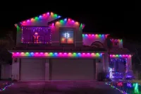 House covered in colorful Christmas lights at night, with illuminated windows and front porch.
