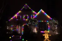 House covered in colorful Christmas lights at night with a glowing reindeer decoration in front