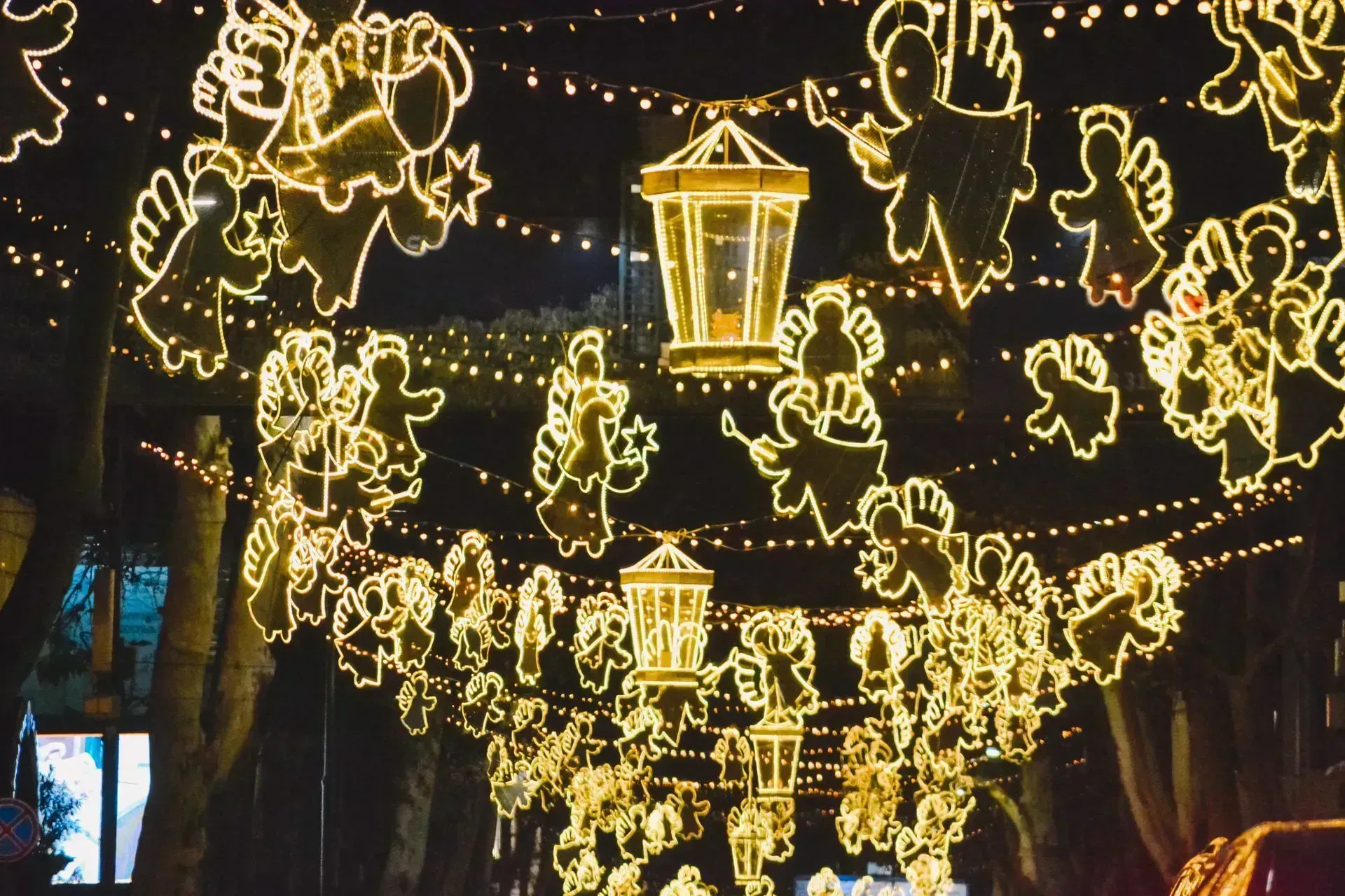 Glowing lanterns and string lights hang over a street at night, forming festive animal shapes and a central lantern