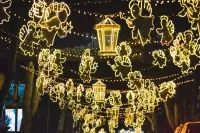 Glowing lanterns and string lights hang over a street at night, forming festive animal shapes and a central lantern