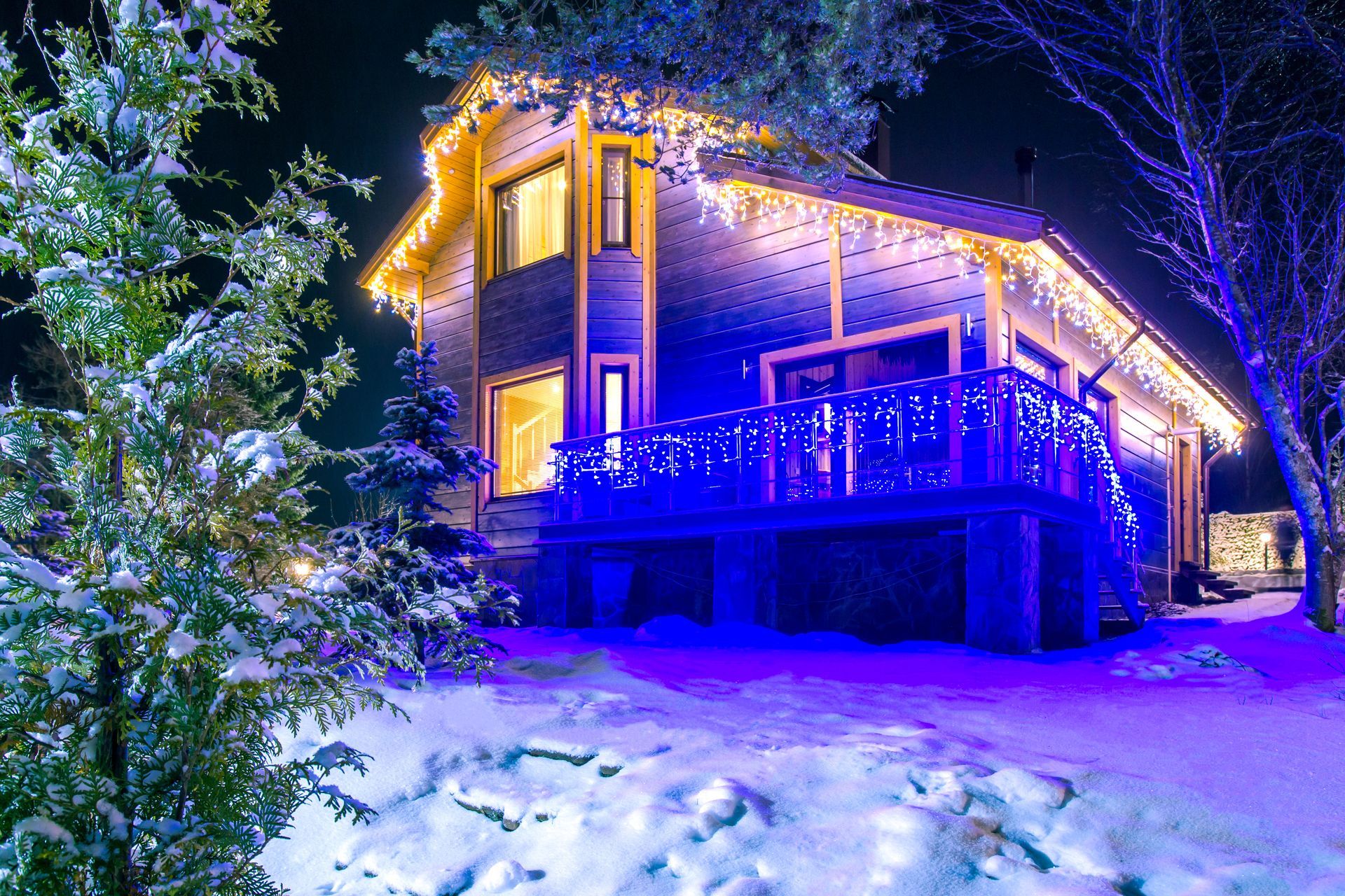 Snow-covered cabin glowing blue and gold at night, surrounded by trees