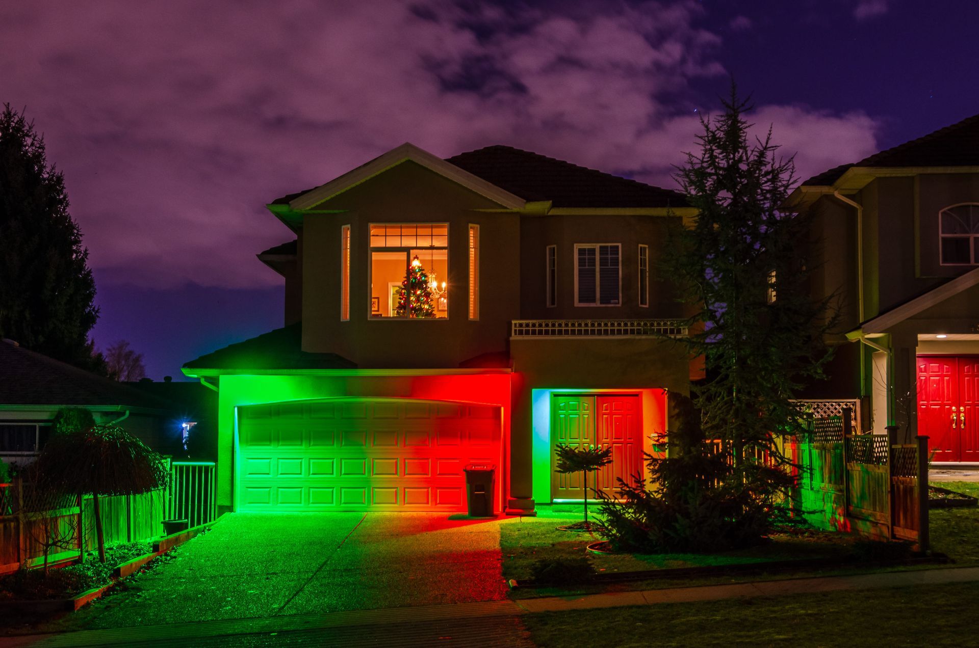 House at night lit with green and red holiday lights, glowing windows, and a purple sky