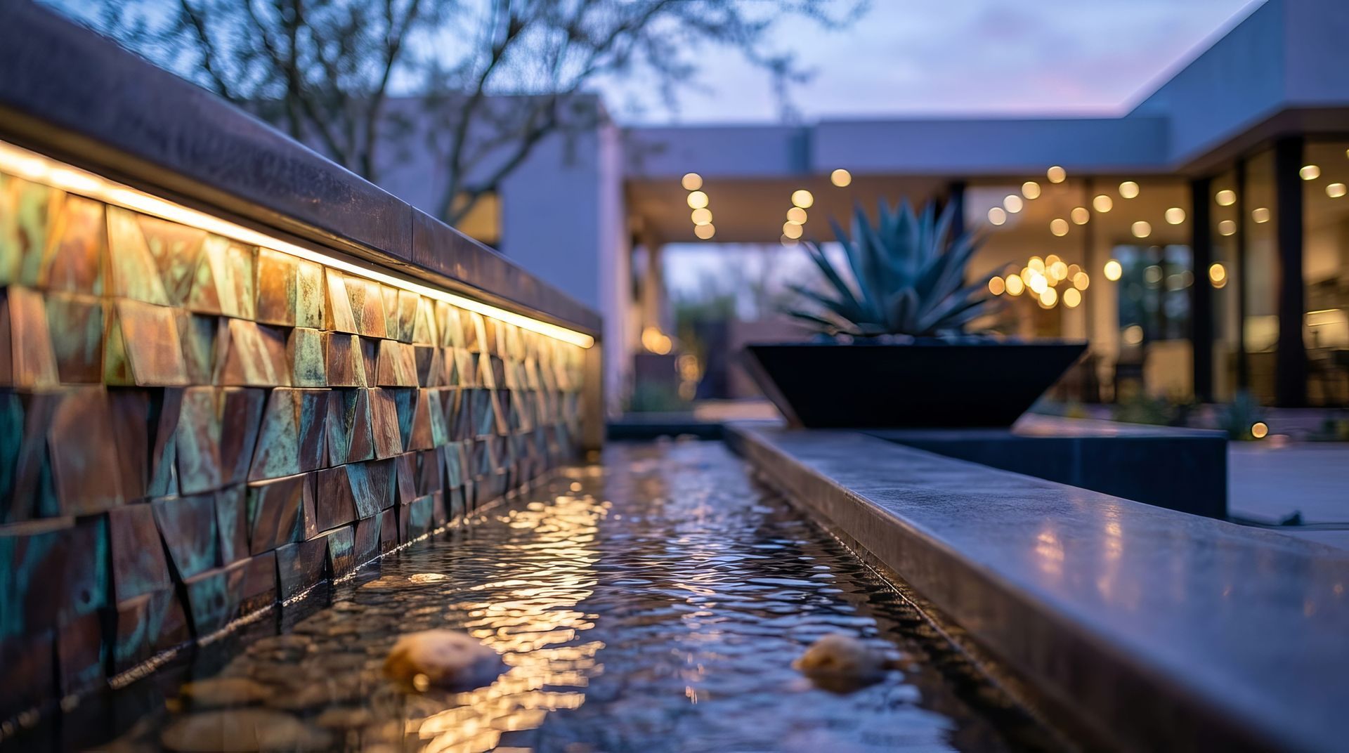 Modern courtyard water feature at dusk with lit stone wall and reflecting pool