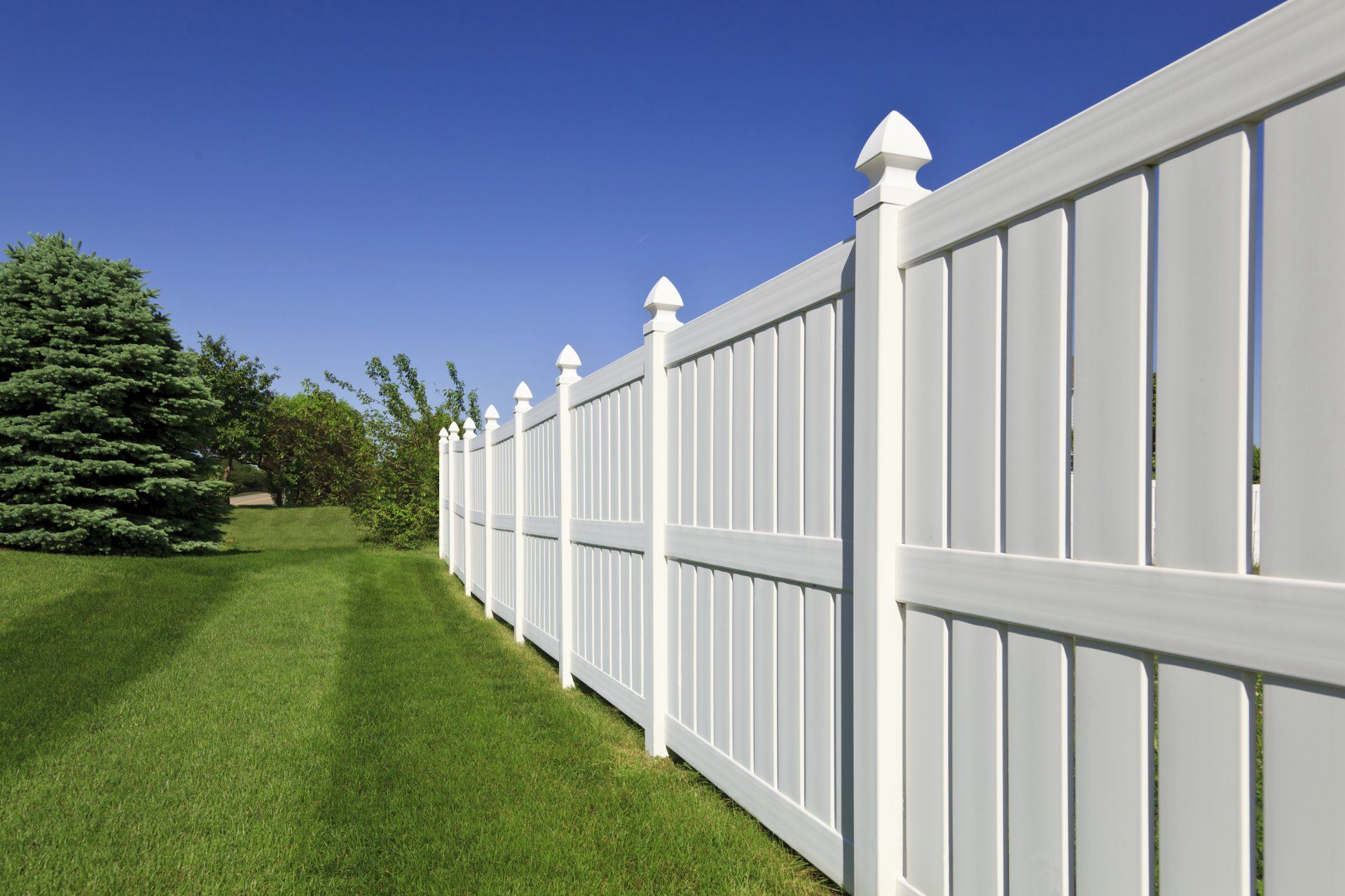 White vinyl fence along green lawn under blue sky.