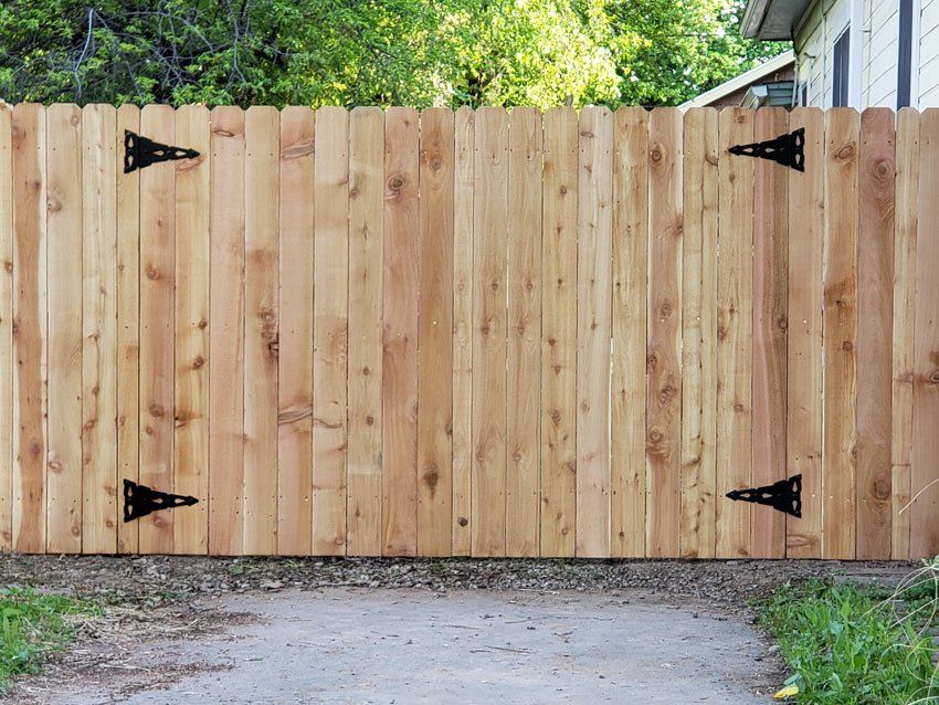 Wooden fence with black hinges, set against a backdrop of trees and a gravel path.