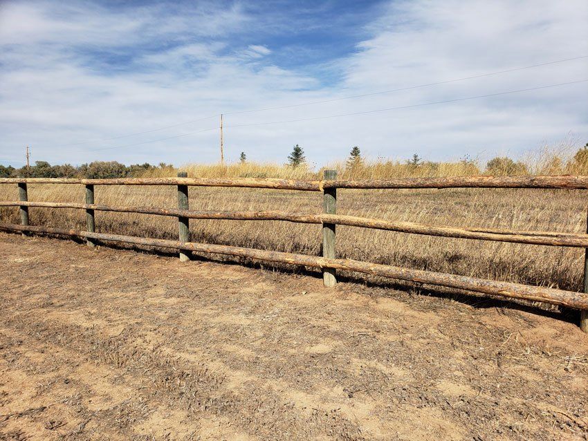 Wooden fence in front of dry field under blue sky with some clouds.