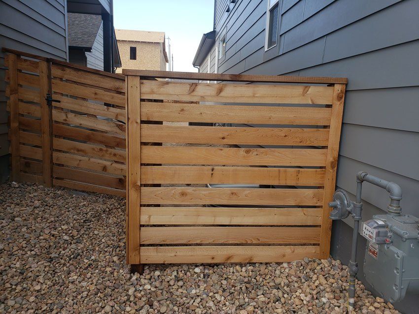 Wooden enclosure around a gas meter, constructed with horizontal slats, gravel ground.