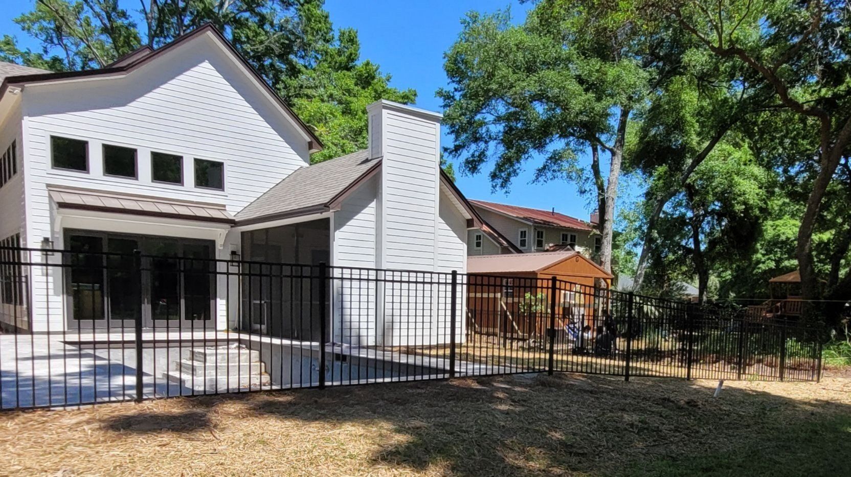 White house with black fence and chimney on a sunny day. Backyard with trees.