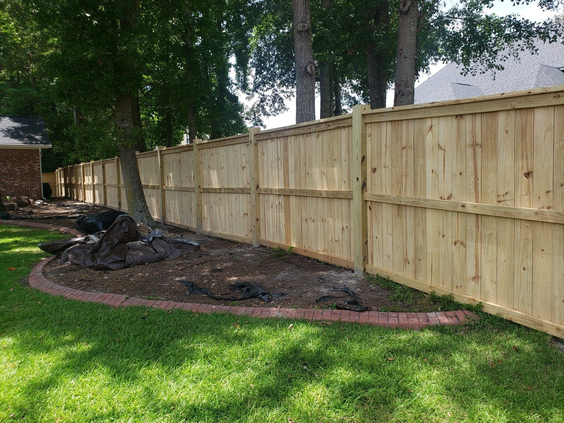 Wooden privacy fence in a grassy yard, with a brick border around a tree.