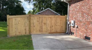 Wooden fence next to a brick building and a concrete driveway on a grassy lawn.