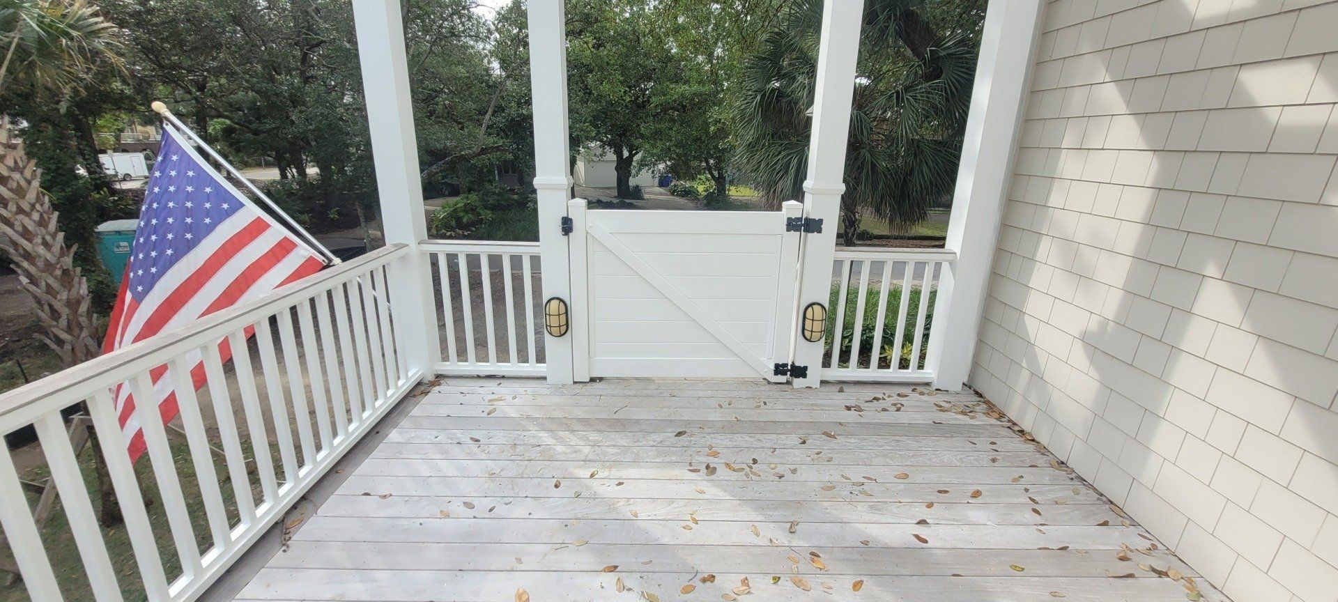 White porch with an American flag, gate, and trees in the background.