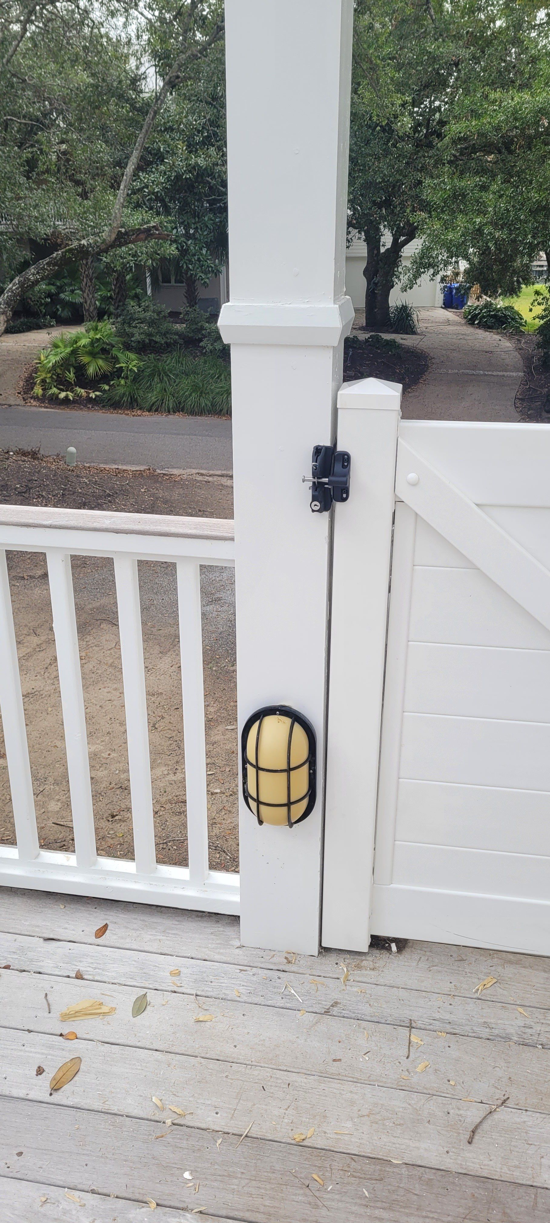 White gate post with black security camera and yellow-caged light fixture.