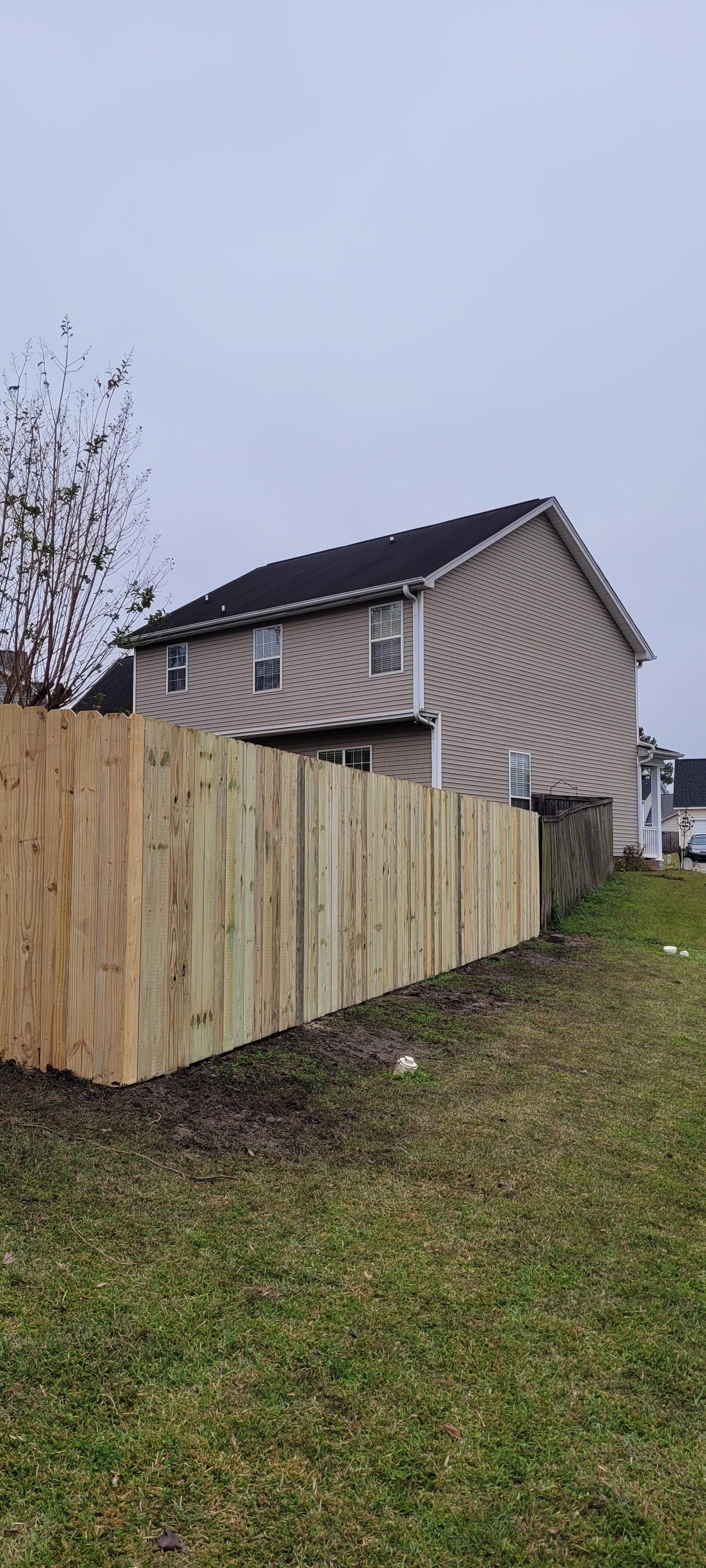 Wooden fence next to a two-story beige house on a cloudy day.